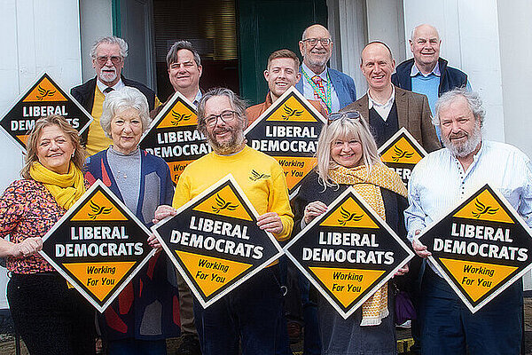 A group of cheerful-looking Liberal Democrats holding diamond posters with the slogan winning for you