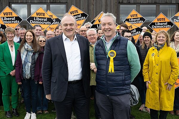 A group of cheerful-looking Liberal Democrats holding diamond posters with Ed Davey in the foreground