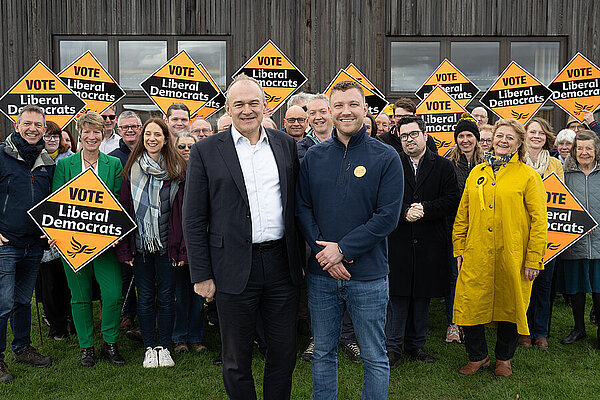 A group of cheerful-looking Liberal Democrats holding diamond posters with Ed Davey in the foreground