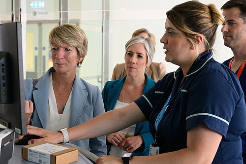 A nurse at Addenbrookes Hospital demonstrates something on a screen to Pippa Heylings, Lib Dem Parliamentary Candidate for South Cambs. Daisy Cooper MP, the national Liberal Democrat Health and Social Care spokesperson, sits behind Pippa looking at the same screen.