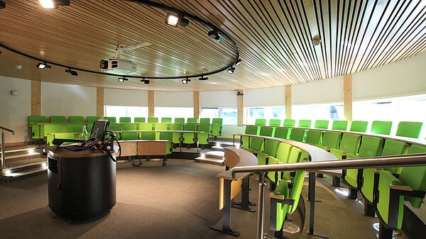 Picture of circular lecture theatre with three rows of green seats in a semi-circle facing a lectern