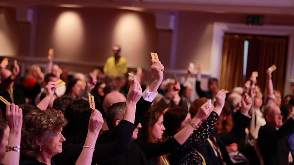 A hall full of conference attendees raising their hands to vote