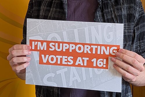 Cllr Nathan Hunt holding a sign that reads "I'm supporting votes at 16!"