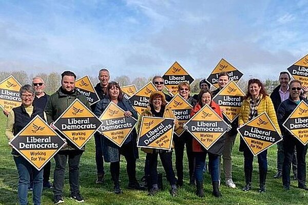 A group of Liberal Democrats holding diamond shaped posters in a field